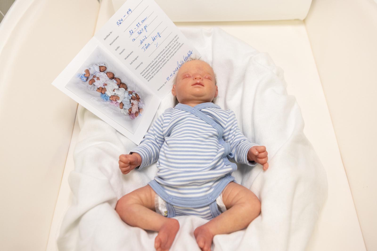 Ein schlafendes Baby in blau-weißem Strampler liegt in einem weißen Bett neben einer geöffneten Geburtskarte.